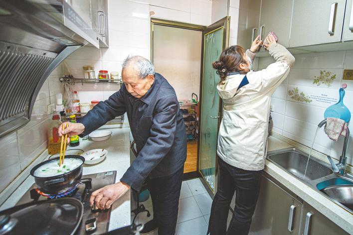 3月7日，吴益寿老人在家煮面条，照护师徐秋红在做卫生。