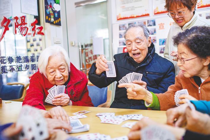 3月26日，黄啟知（左二）与邻居们玩牌，照护师李丹君在他身后观看。